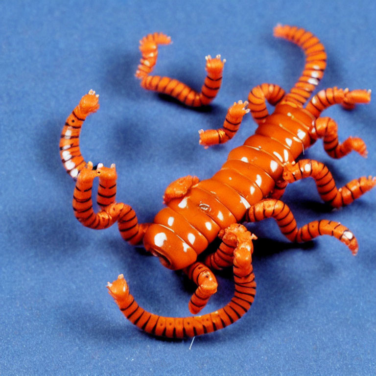 Orange Toy Scorpion with Articulated Limbs on Blue Background