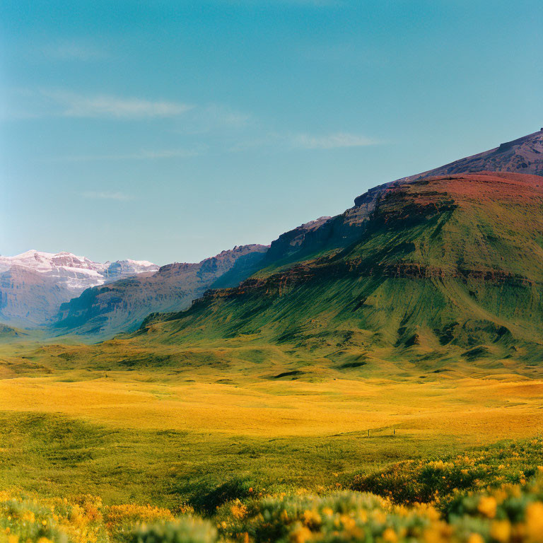 Scenic landscape: green meadows, rolling hills, rocky mountain, blue sky