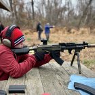 Person in red beanie aiming sniper rifle in snowy futuristic cityscape