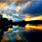 Sunset oil painting: vivid orange clouds reflected on tranquil forest lake