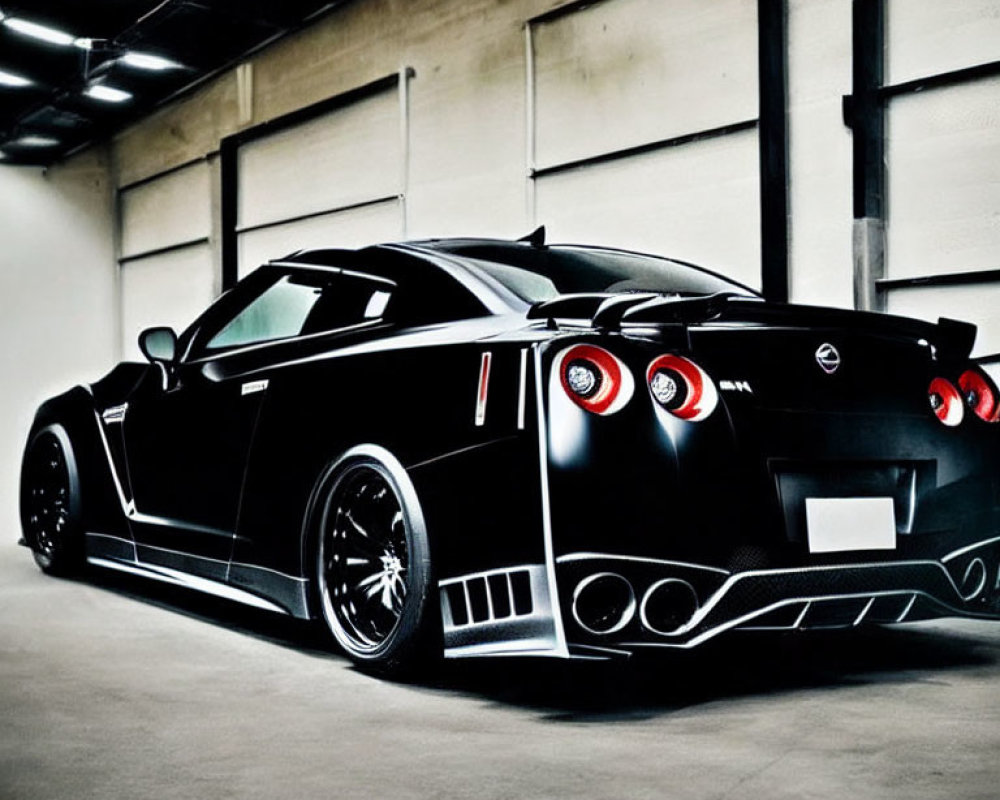 Black Nissan GT-R with spoiler and custom wheels in dimly lit garage