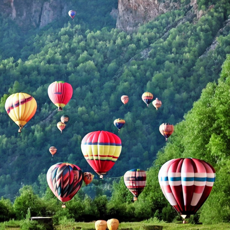 Vibrant hot air balloons soar over green hills and mountains under a pale blue sky