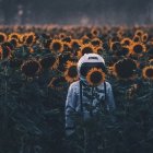 Astronaut in purple suit among sunflowers under twilight sky