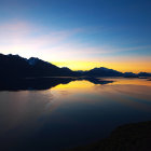 Panoramic sunset over mountain lake with blue and orange skies.