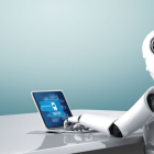 White humanoid robot at desk with blue laptop on teal background