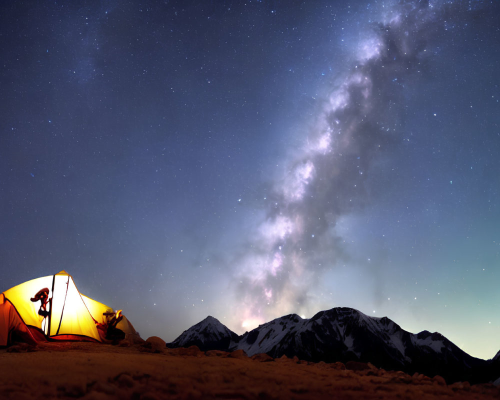 Silhouetted person under glowing tent with starry sky and Milky Way over dark mountains.