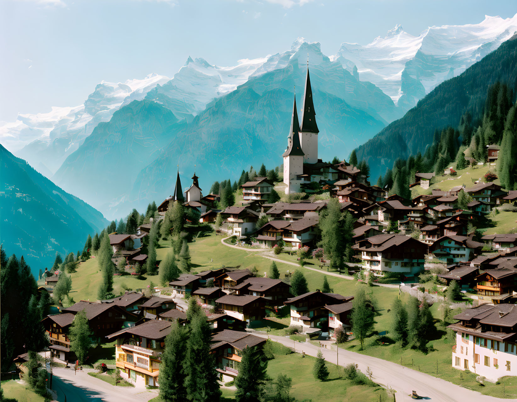 Scenic mountain village with chalet houses, church spire, greenery, snow-capped peaks