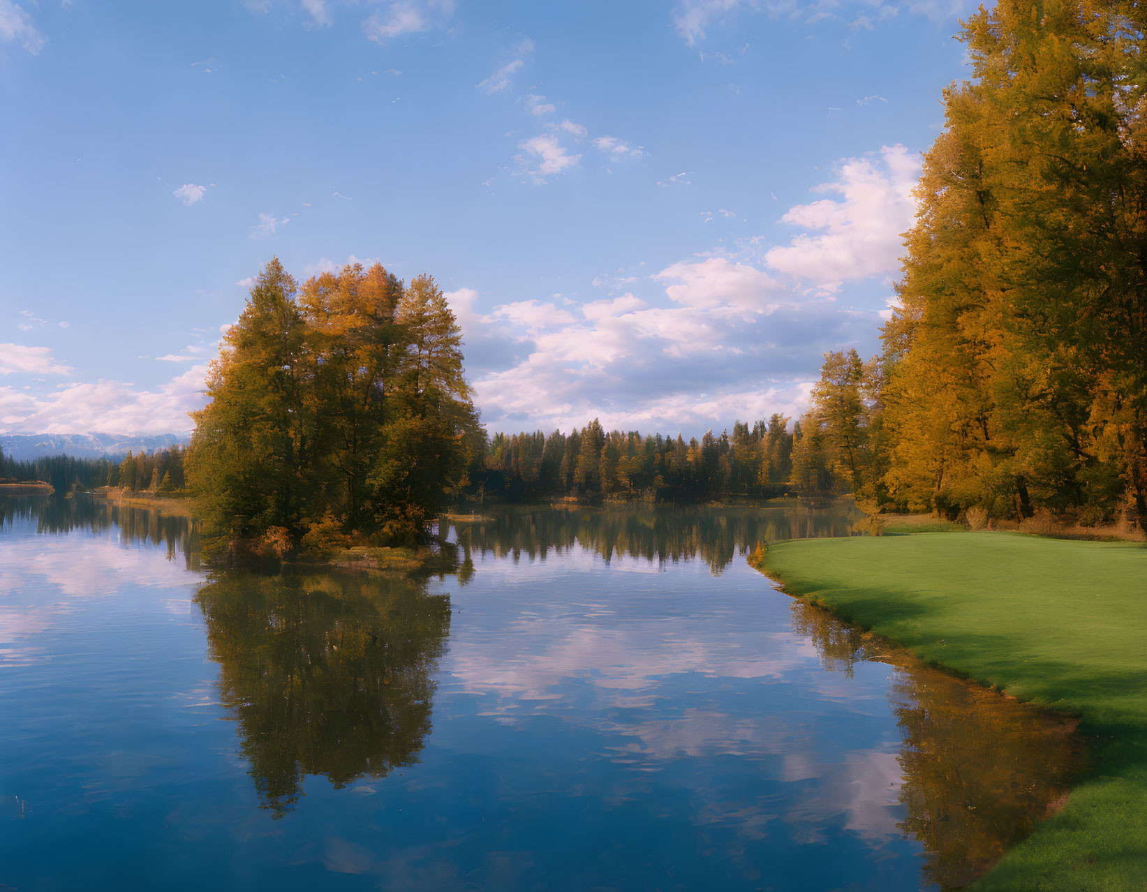 Autumn trees reflected in tranquil lake under clear blue sky