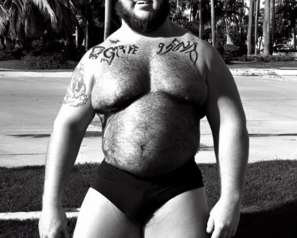 Bearded Man with Tattoos Outdoors in Black Underwear, Palm Trees Background