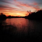 Dramatic sunset over dark rocky shoreline with vibrant clouds