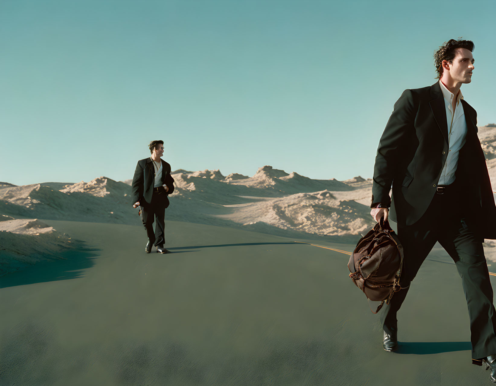 Two men in business suits with a duffle bag walking in desert landscape