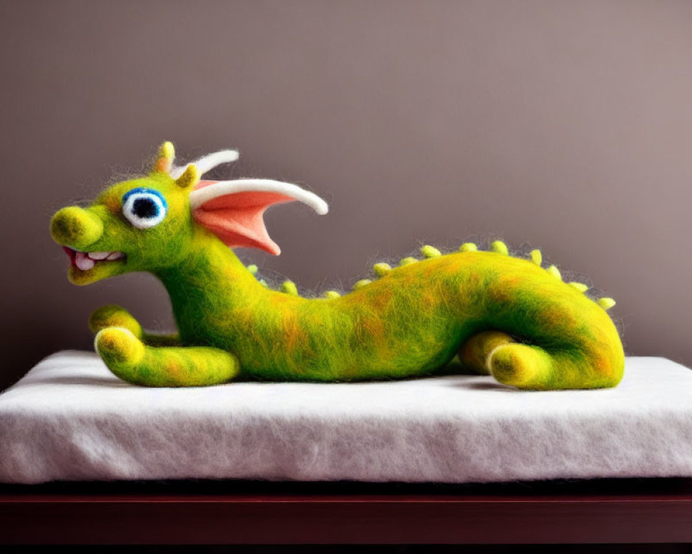 Colorful Felt Dragon with Big Eyes and Wings on Cushion and Wooden Surface