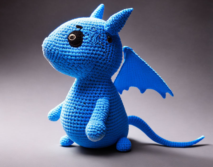 Blue Crocheted Dragon Toy with Big Eyes, Wings, and Tail on Grey Background