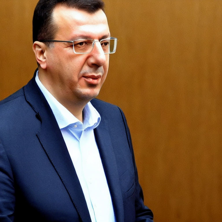 Serious man in glasses with dark suit and blue shirt on wooden background