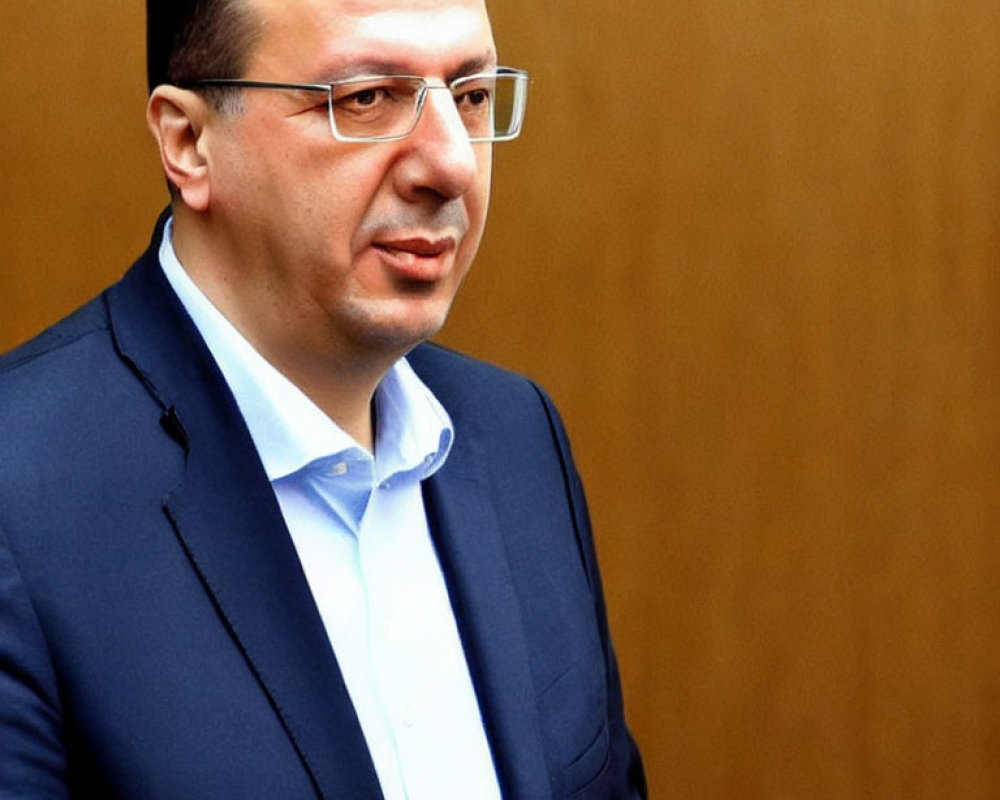 Serious man in glasses with dark suit and blue shirt on wooden background