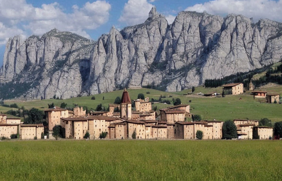 Scenic village with uniform buildings, church spire, lush field, and towering mountains