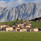 Scenic village with uniform buildings, church spire, lush field, and towering mountains