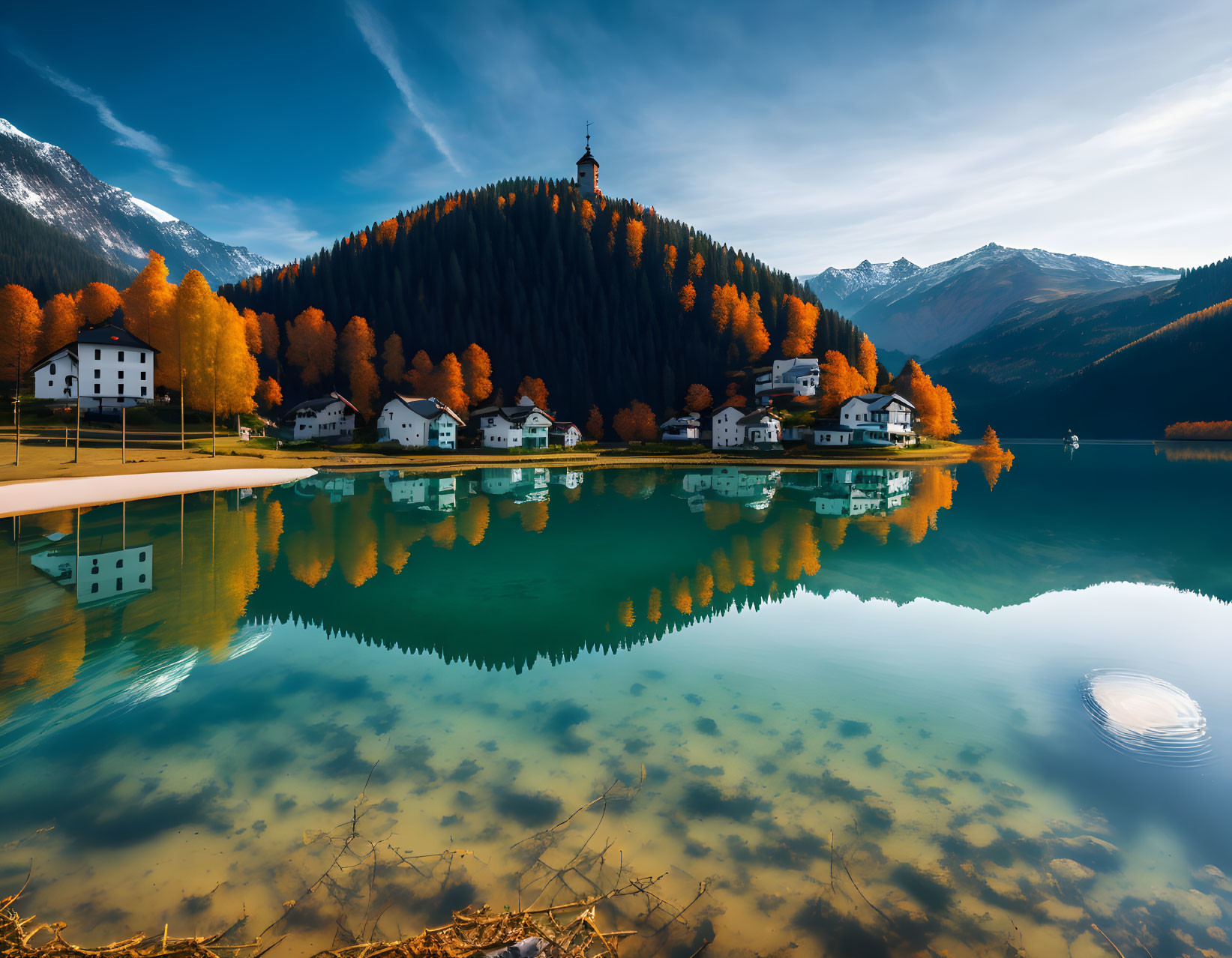 Tranquil alpine lake reflects autumn village and snowy mountains