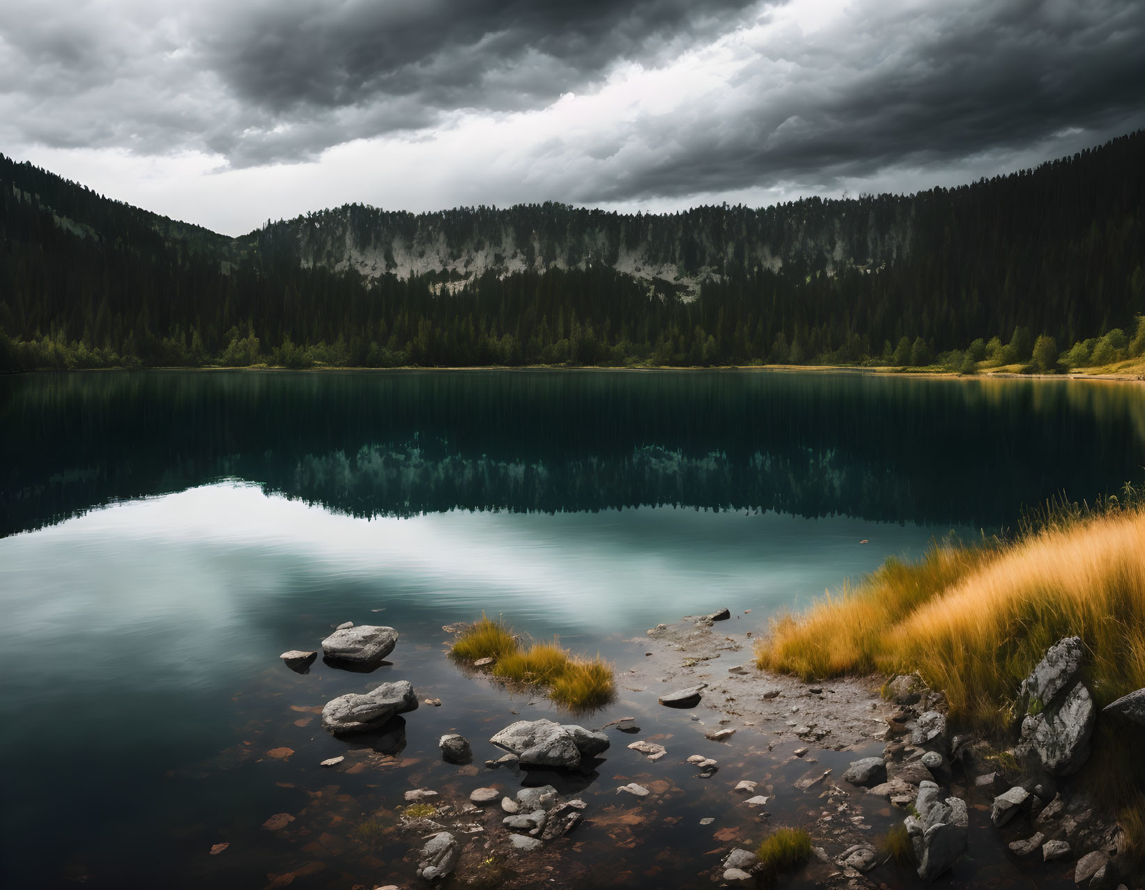 Serene lake, clear reflections, forested mountains, dramatic sky