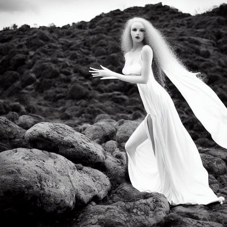 Monochrome image of person with voluminous hair in flowing white dress on rugged terrain