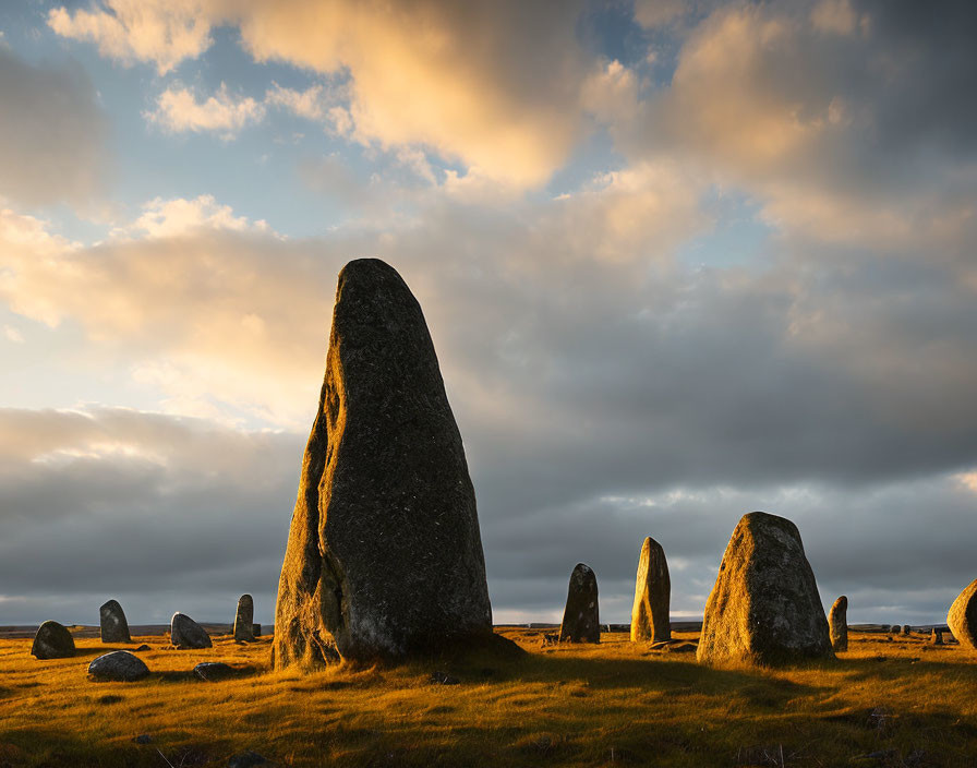 Ancient standing stones under dramatic sunset sky with long shadows.