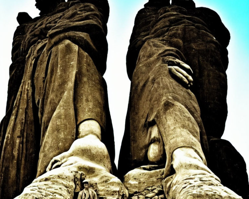 Person sitting at base of large stone statues under clear sky