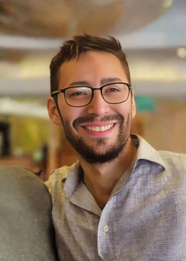 Smiling man with glasses in gray shirt indoors