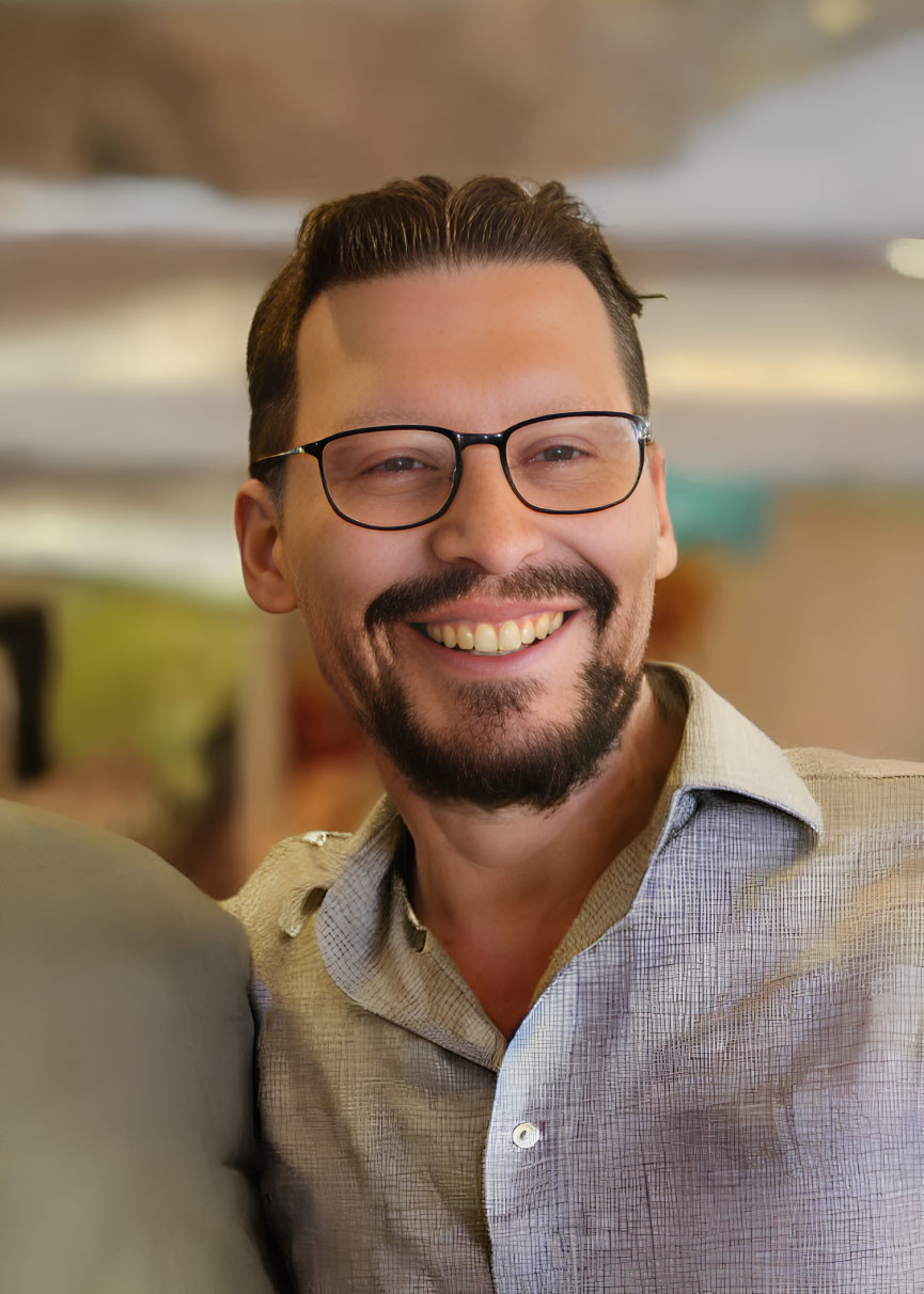 Smiling man with glasses, beard, and mustache in gray shirt