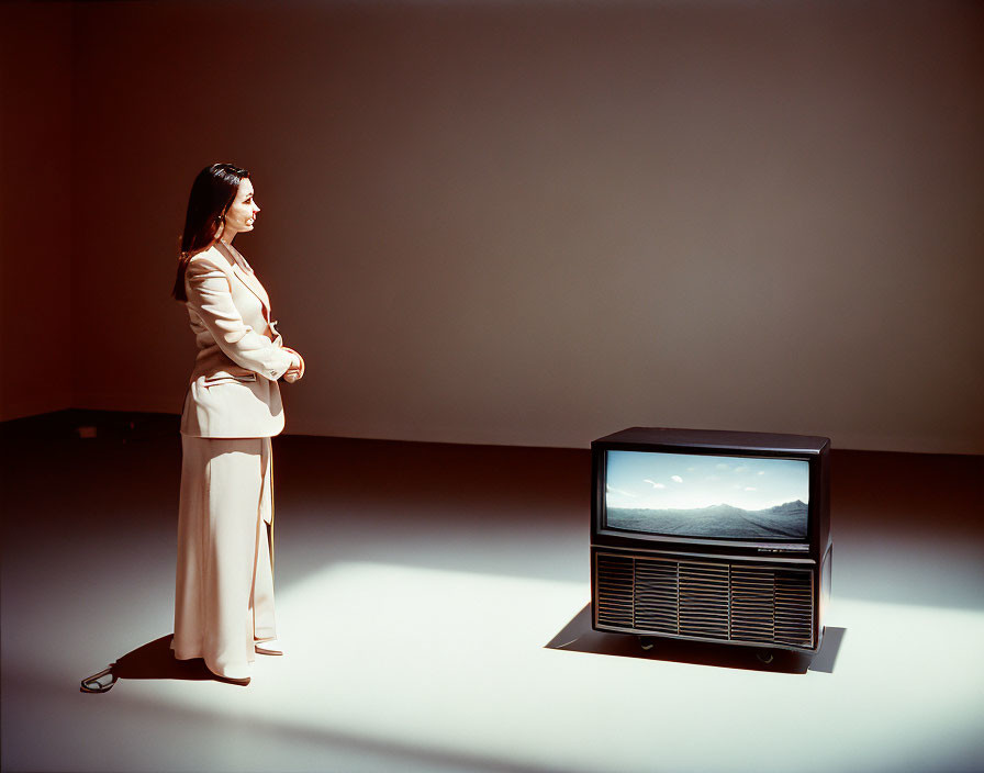 Woman in beige suit gazes at mountain scene on old TV