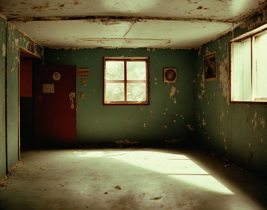 Abandoned room with peeling green walls, red door, window, old signs, and clock