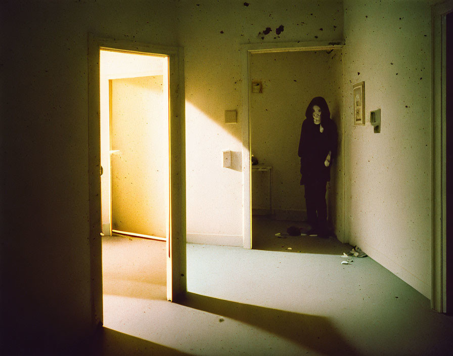 Abandoned room with figure in black hoodie by open door