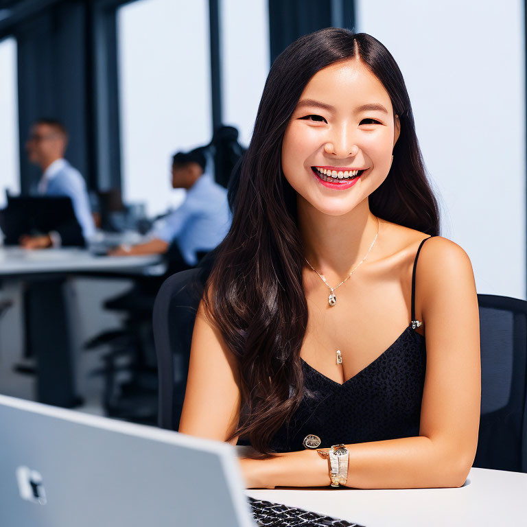 Smiling woman at desk with laptop and coworkers in background