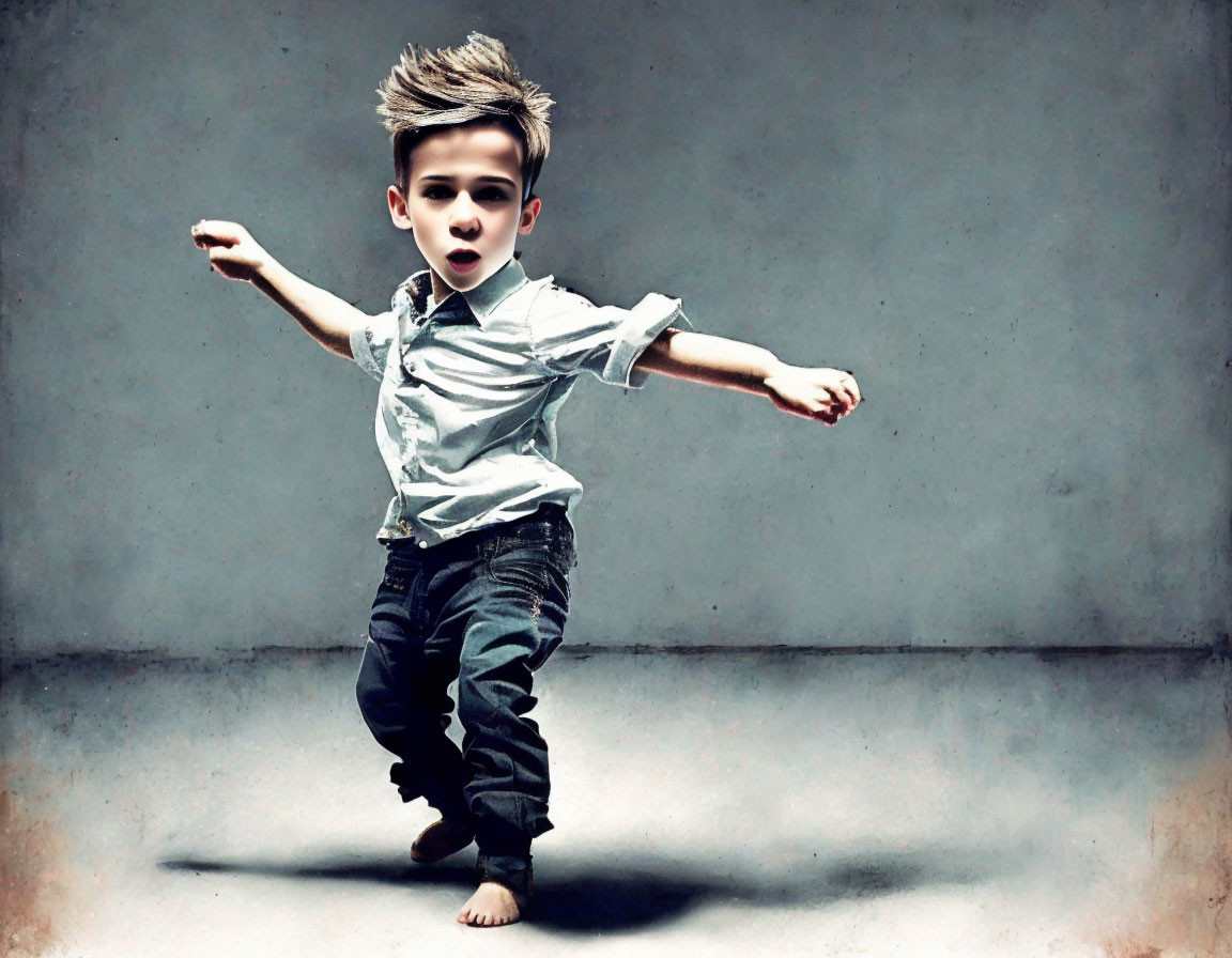 Stylish young boy in blue shirt and jeans dancing on grey backdrop