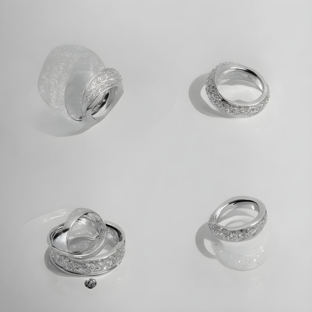 Four silver rings with intricate designs and diamonds on reflective white surface