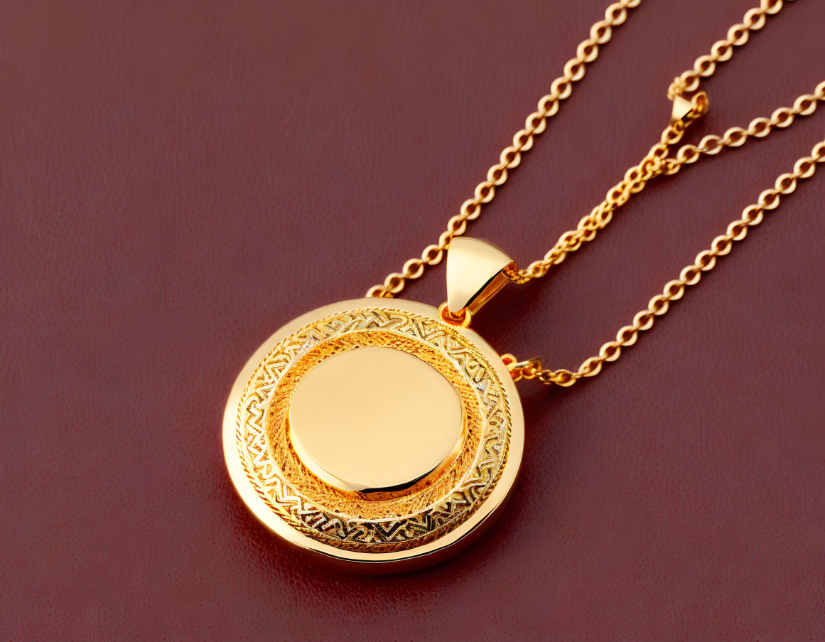 Gold locket pendant on matching chain with intricate designs on maroon background