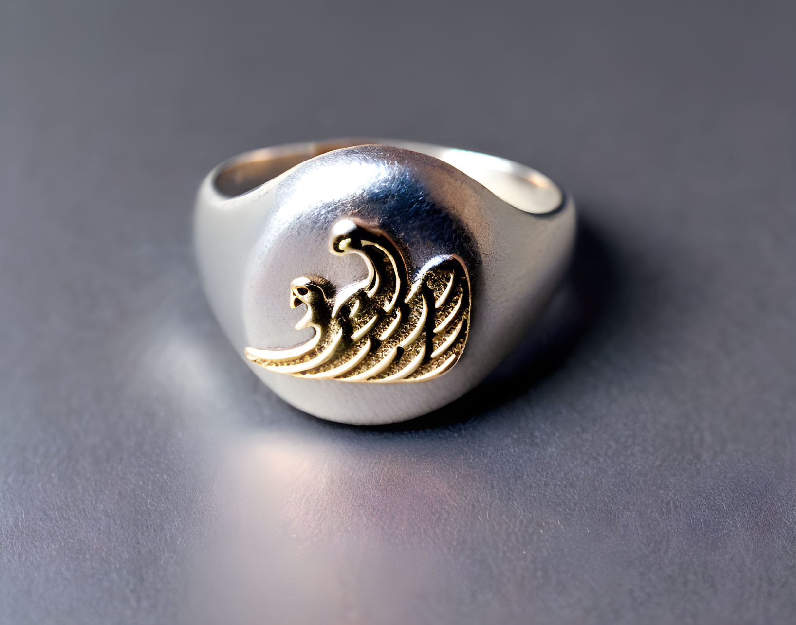 Silver ring with gold inlay featuring flame/wave design on textured grey surface