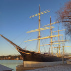 Tall ship with multiple masts in calm waters at sunset and cherry blossom branch overhead