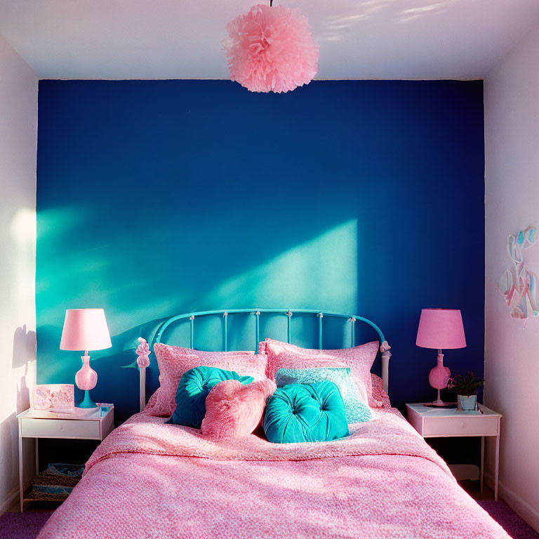 Pink bedding and pillows in bedroom with pink lamps on nightstands, against blue accent wall.