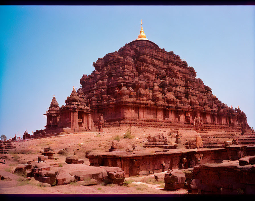 Ancient multi-tiered temple with golden spire in rocky terrain