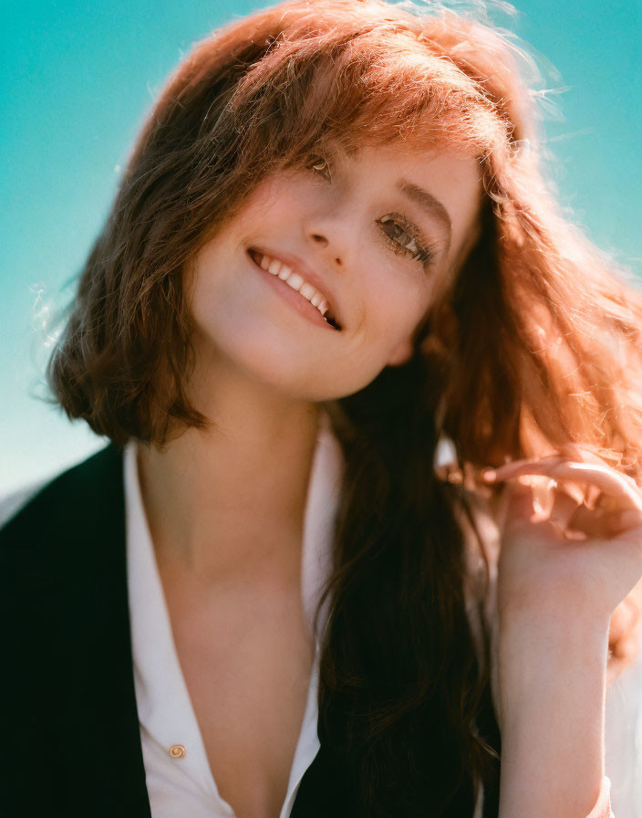 Red-haired woman in black blazer smiles on teal background