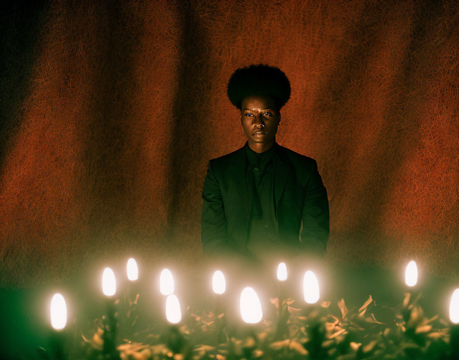 Person with Afro Hairstyle Standing Among Candles in Dark Blazer on Red Textured Background