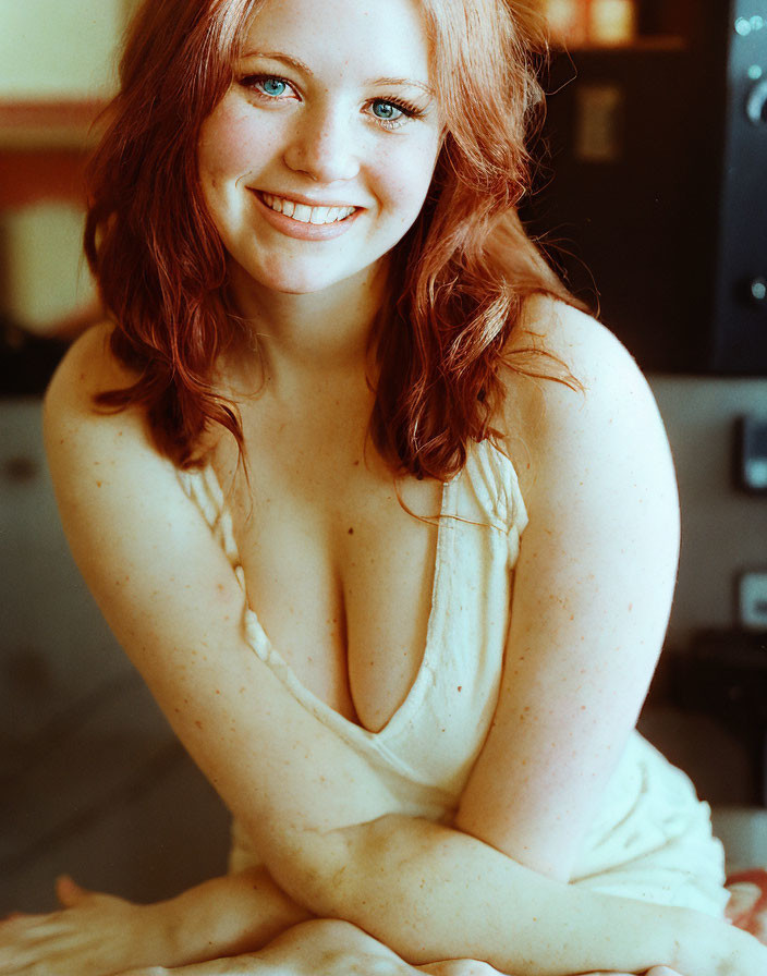 Red-haired woman with blue eyes in sleeveless top seated indoors