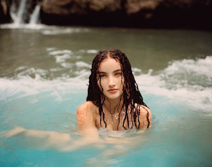 Young woman with wet hair emerges from turquoise water in natural backdrop