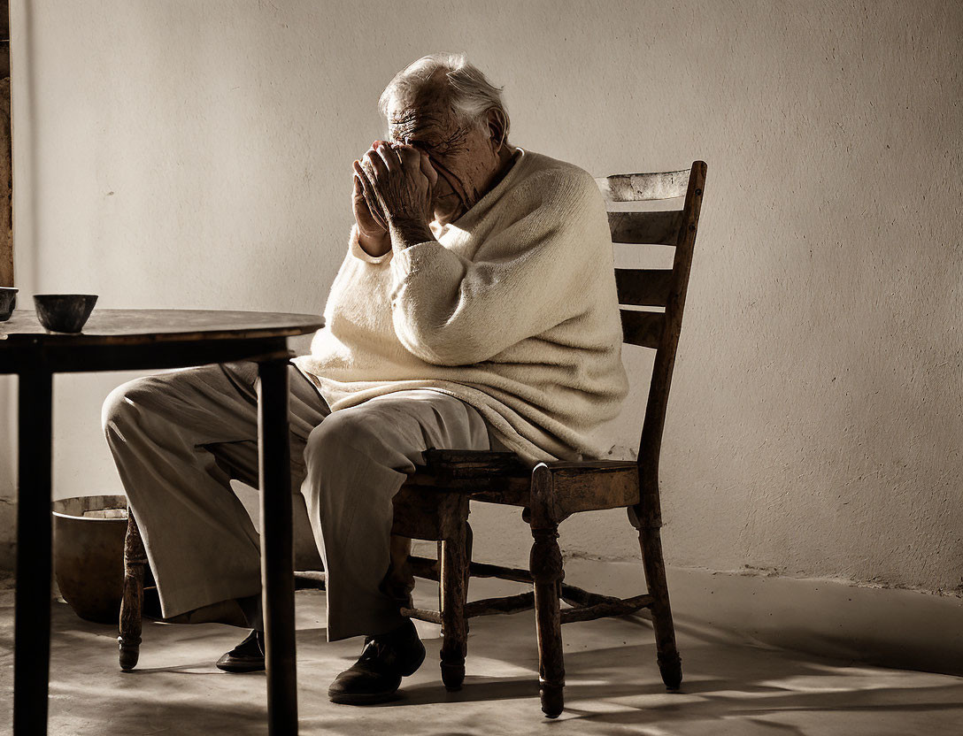 Elderly person sitting on wooden chair in dimly lit room