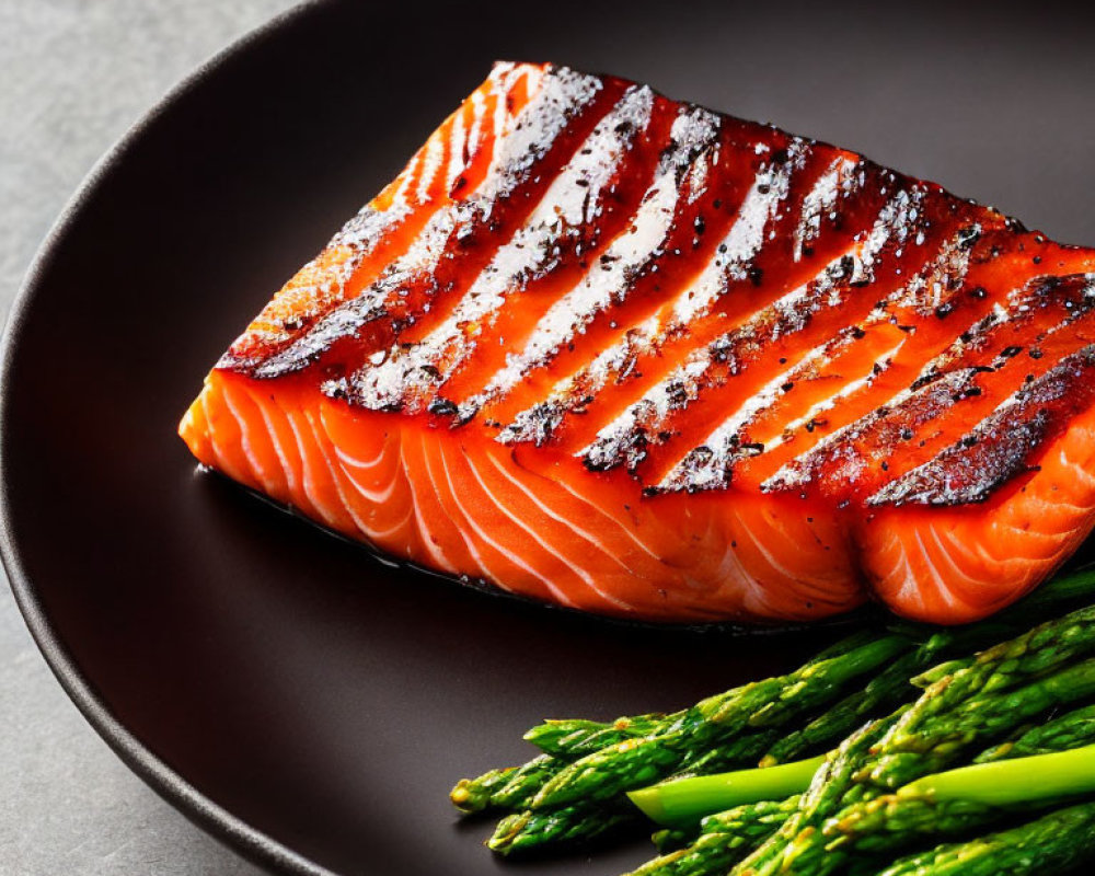 Grilled Salmon Fillet with Charred Grill Marks on Black Plate with Green Asparagus on Grey Background