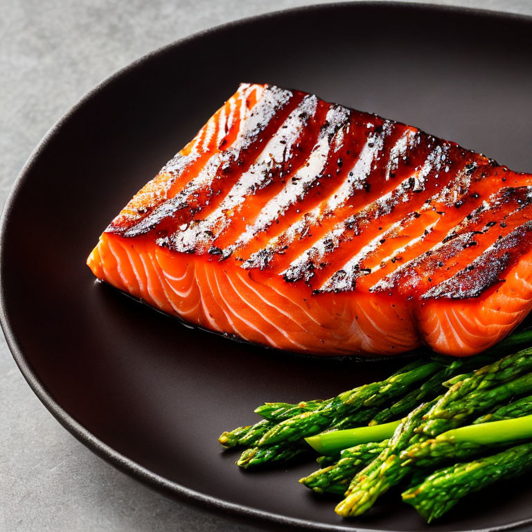 Grilled Salmon Fillet with Charred Grill Marks on Black Plate with Green Asparagus on Grey Background