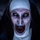 Pale-faced nun figure with dark eyes and blood around mouth.