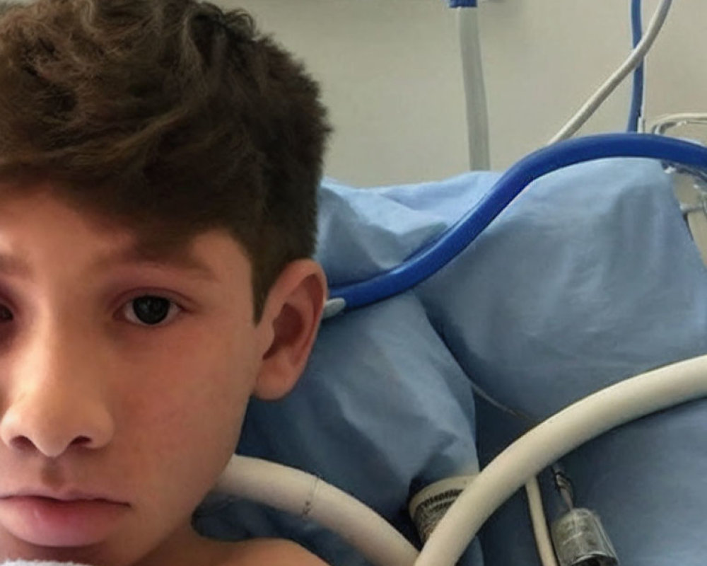 Young boy in hospital bed surrounded by medical equipment and tubes.