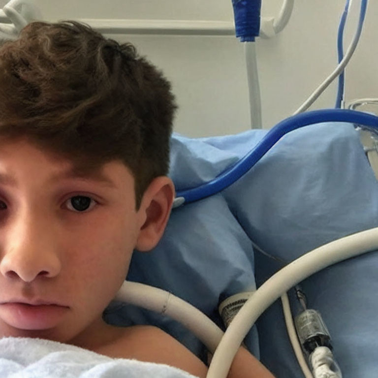 Young boy in hospital bed surrounded by medical equipment and tubes.