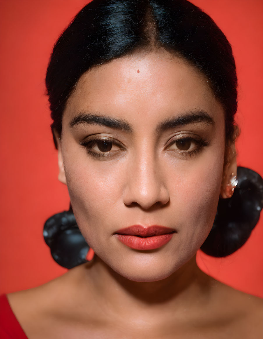 Close-up portrait of woman with sleek hair, red lipstick, and large round earrings on red background